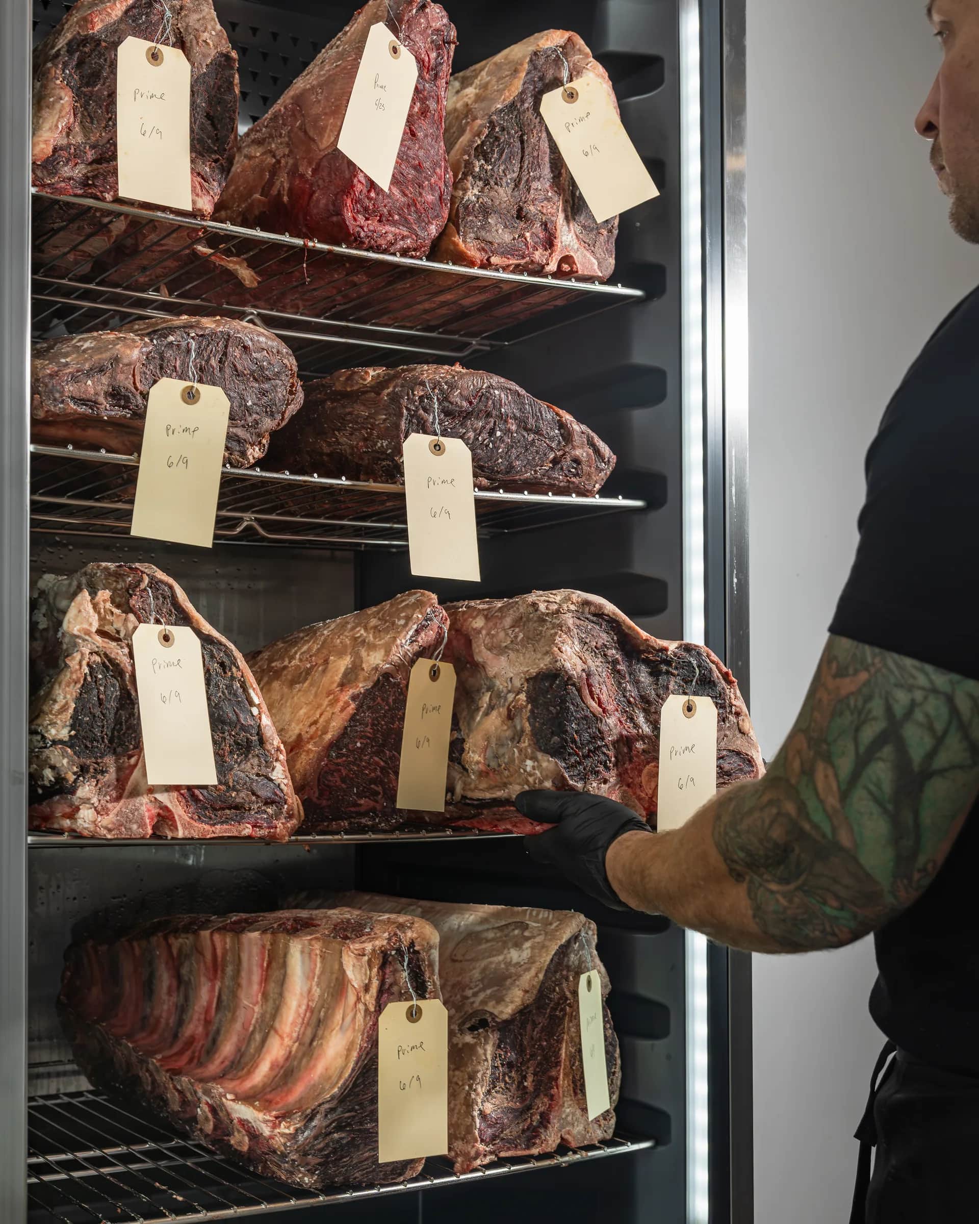 Butcher pulling a tagged dry-aged cut from the cabinet