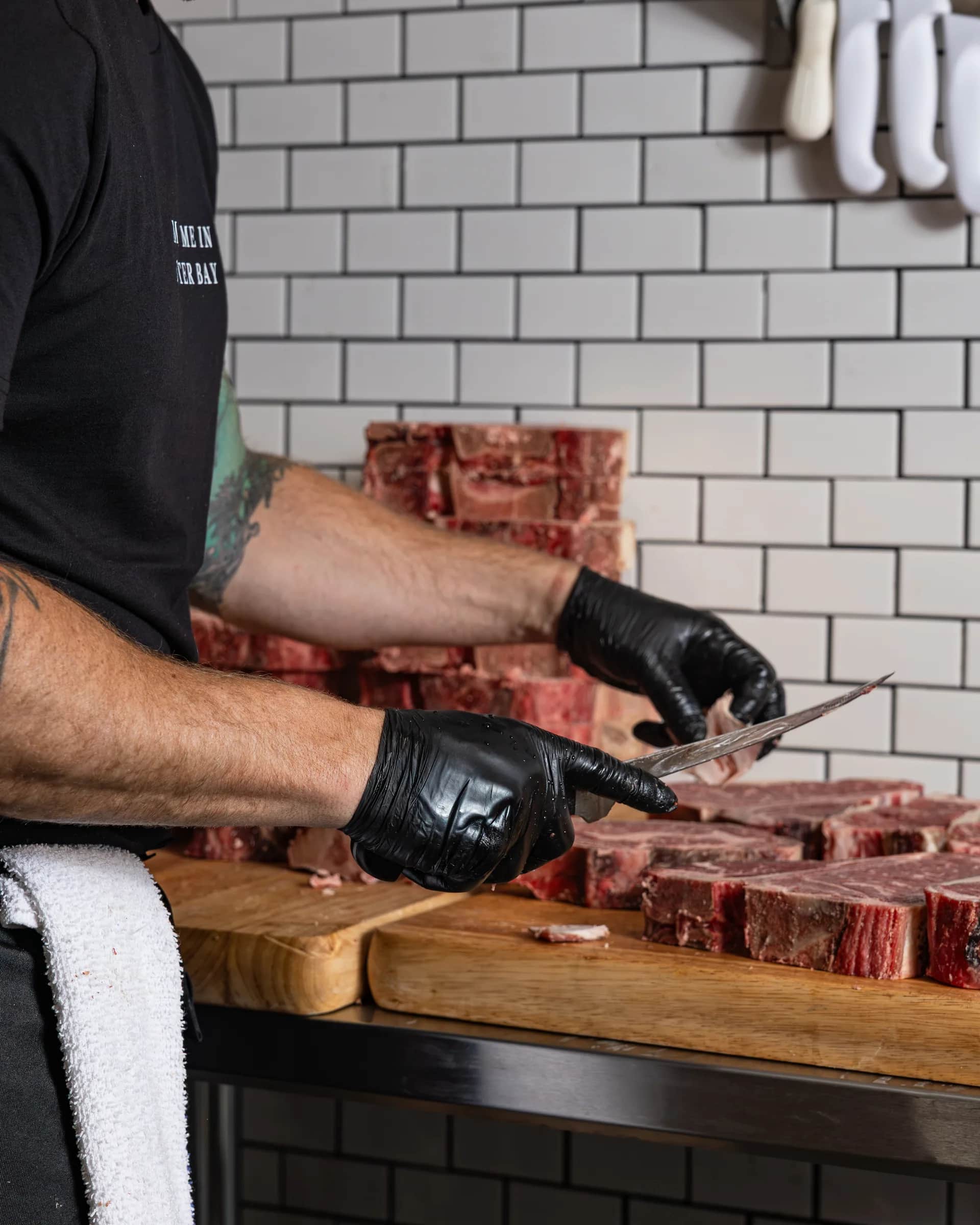 Gloved hands slicing a steak on the wooden board