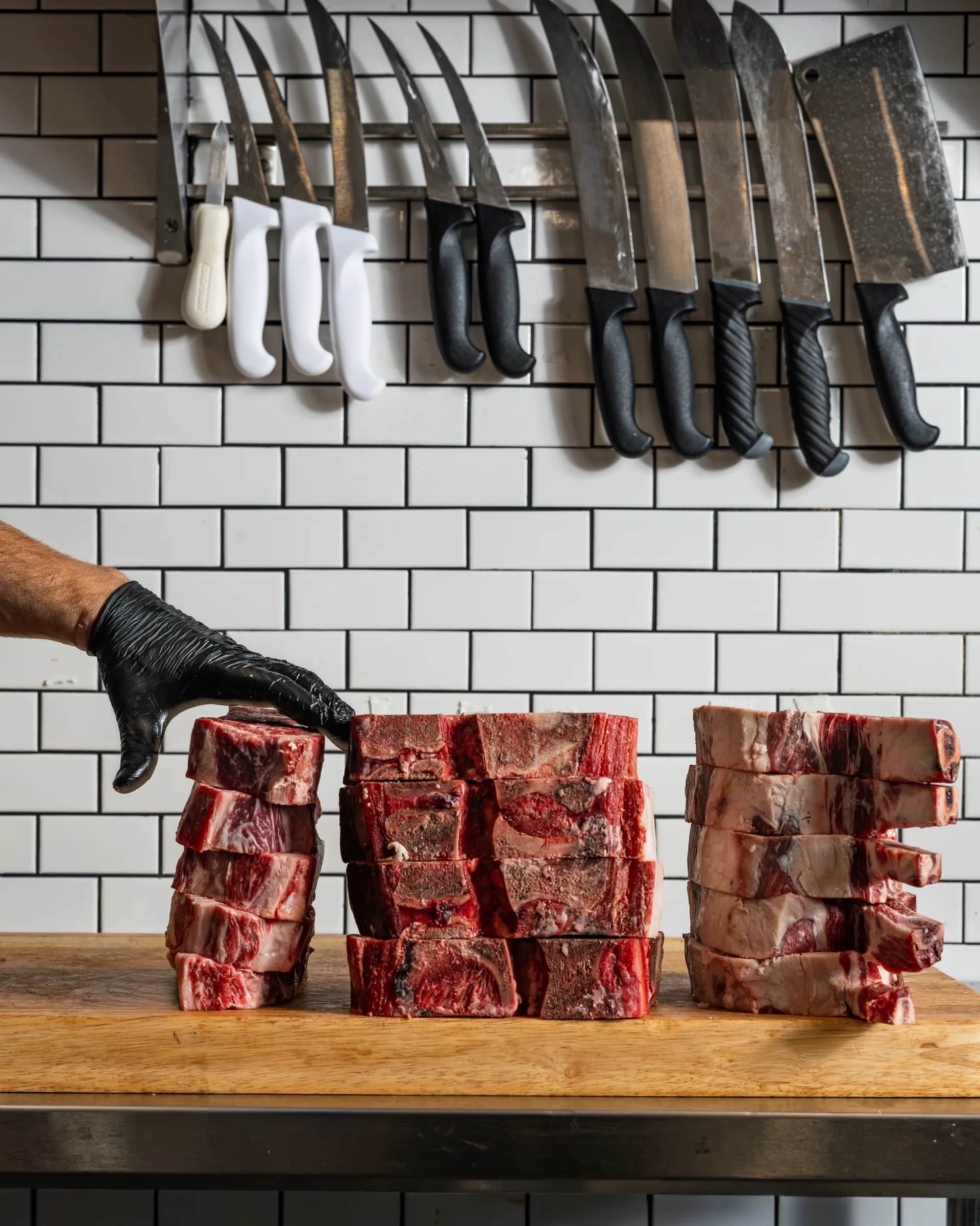 Gloved hand steadying stacked short ribs beneath the knife rack